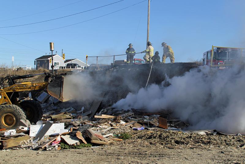 Waste facility mployees use a front-end loader, left, to dig into the burning demo pile so water can penetrate and put it out the fire. (Photo courtesy Rockland Fire Department/by Alan Athearn)