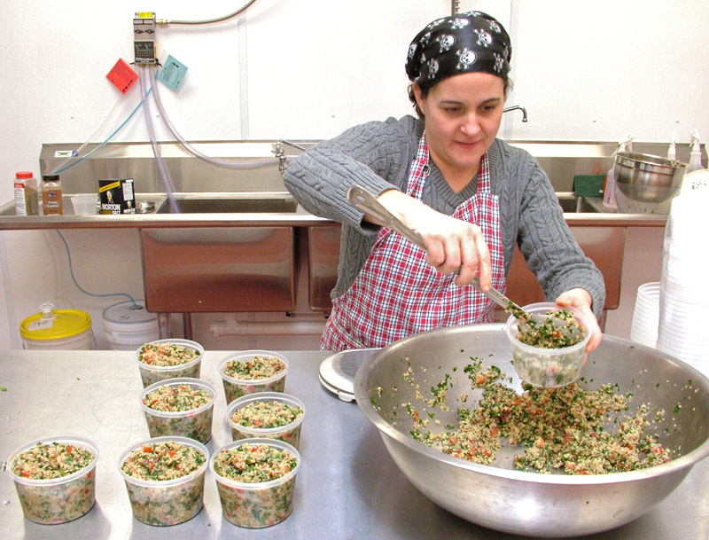 Julie Romano, of Julie Ann's Outrageous! Foods, fills containers with quinoa tabouli in the commercial kitchen space she rents at Coastal Farms Food Processing. (Photo by Ethan Andrews)