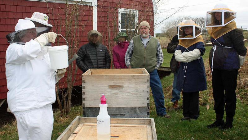 During a KLCBee Club hive installation April 20, Jean Vose shows everyone a feeder bucket filled with sugar water for the bees. (Photo by Holly S. Edwards)