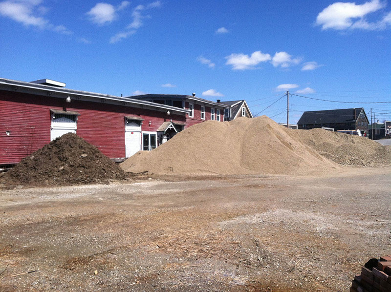Piles of mulch, sand and rough fill on Sunday obscured the city-owned building most recently home to the Belfast Maskers. The property is being used as a staging area for materials for the Belfast Harbor Walk project, which broke ground last week. (Photo by Ethan Andrews)