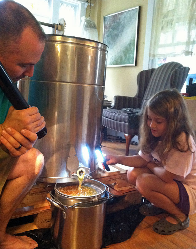 Uncle Dave and Kyra watch the honey flow out of the extractor Sunday. (Photo by Holly S. Edwards)