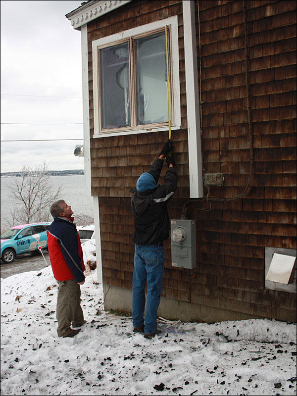 From left, Jack Driscoll and David Cameron measure a window on Driscoll’s home next to the cottage that burned. The men were heading out Tuesday morning to buy plywood to board up their windows that broke in the fire. (Photo by Holly S. Edwards)