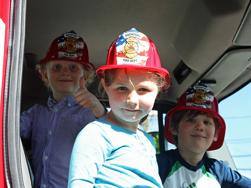 From left, Baxter Thackeray, 4, Charlotte Thackeray, 7, and Calder Meil, 6, enjoy sitting in the front seat of a fire engine during Rockport Public Library’s 100th anniversary celebration May 30. (Photo by Holly S. Edwards)