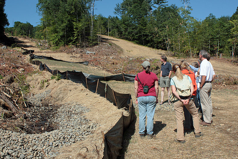 Maine Dept. of Environmental Protection Licensing and Compliance Manager Dawn Hallowell, far left, looks up the newly hay-covered Ragged Mountain slopes, which also have a series of water bars and silt fencing in place. (Photo by Holly S. Edwards)