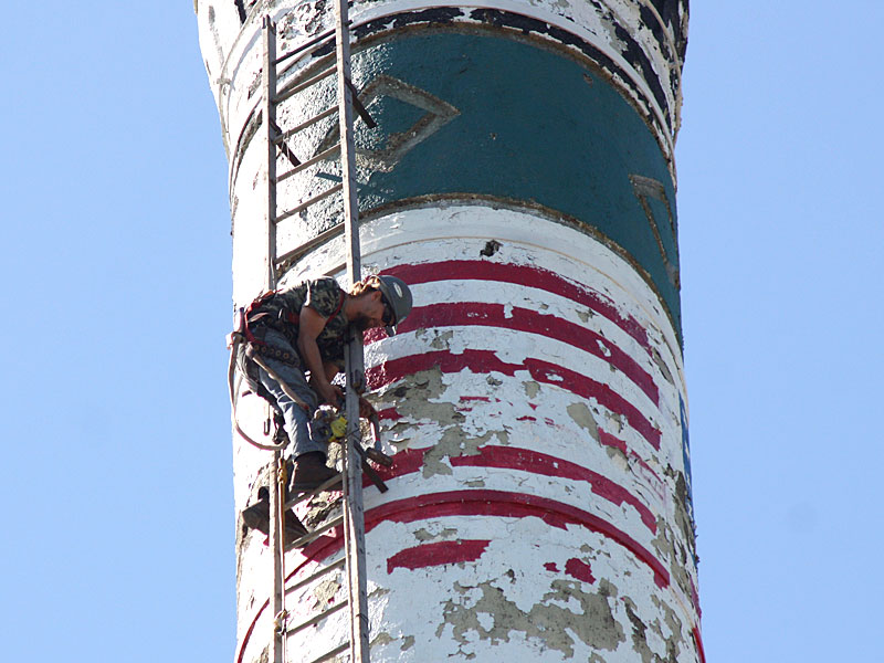Dustin Frazier, of Gibraltar Chimney International, pulls up a lag bolt drill on a rope while attaching 170-feet of ladder to the exterior of the Knox Mill smokestack Tuesday morning. (Photo by Holly S. Edwards)