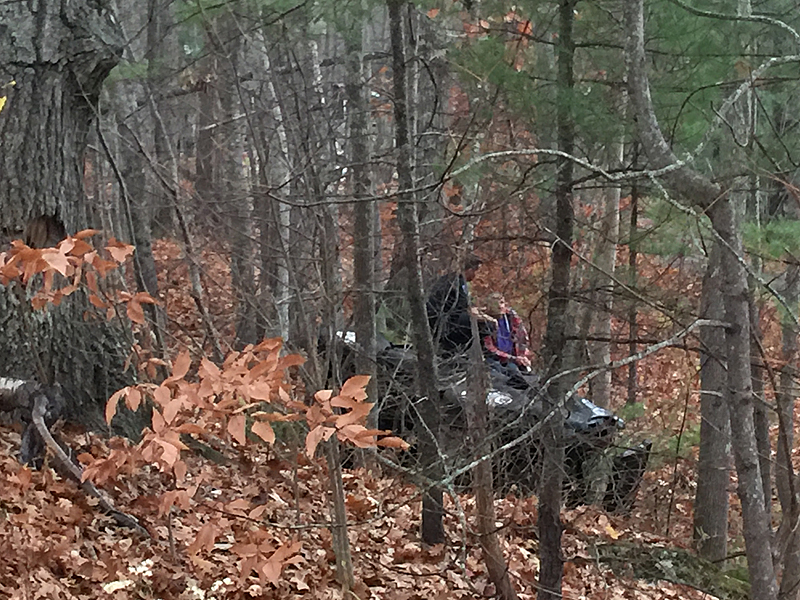 Camden Police Officer Allen Weaver Jr. kneels on top of an overturned pickup truck alongside Guyer ‘Gordon’ Guist, the driver, following a crash over a rock ledge and into the woods off Route 105 late Wednesday afternoon. (Photo by Holly S. Edwards)