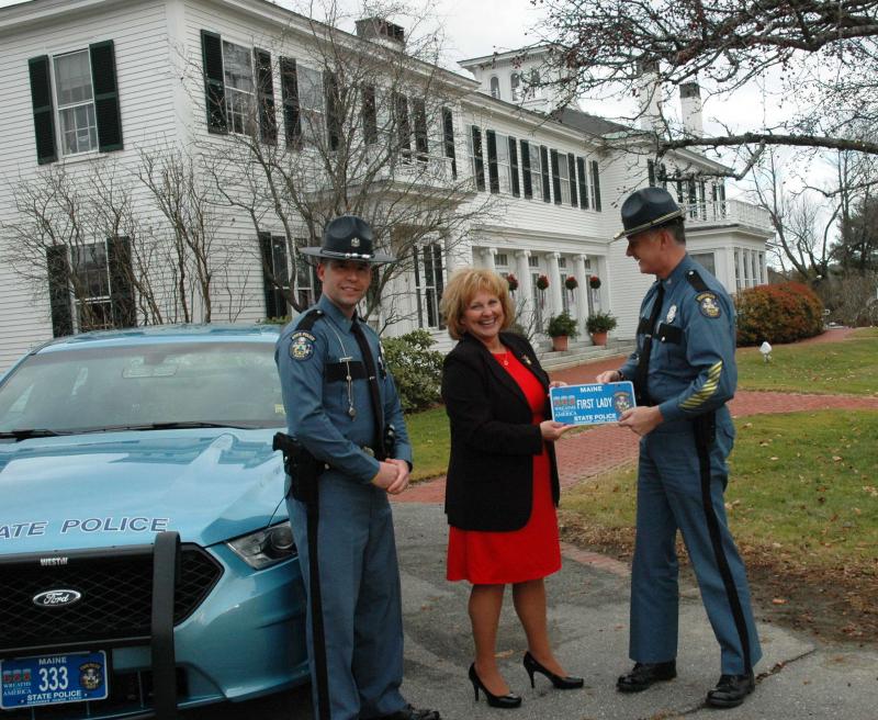 First Lady Ann LePage is presented with her own commemorative license plate outside the Blaine House by the Chief of the State Police, Colonel Robert Williams. The President of the Maine State Troopers Association, Trooper Aaron Turcotte looks on.
