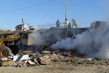 Waste facility mployees use a front-end loader, left, to dig into the burning demo pile so water can penetrate and put it out the fire. (Photo courtesy Rockland Fire Department/by Alan Athearn)