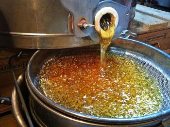 Honey harvested from four frames, removed last week from two of our honeybee hives, flows out of a hand-cranked extractor into a pair of sieves and a collection pot Sunday afternoon, Sept. 22. The white flecks are pieces of honey comb, scratched open to remove the surface caps. (Photo by Holly S. Edwards.)