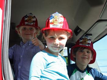 From left, Baxter Thackeray, 4, Charlotte Thackeray, 7, and Calder Meil, 6, enjoy sitting in the front seat of a fire engine during Rockport Public Library’s 100th anniversary celebration May 30. (Photo by Holly S. Edwards)