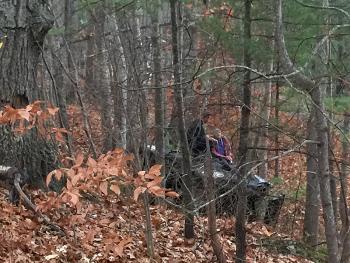 Camden Police Officer Allen Weaver Jr. kneels on top of an overturned pickup truck alongside Guyer ‘Gordon’ Guist, the driver, following a crash over a rock ledge and into the woods off Route 105 late Wednesday afternoon. (Photo by Holly S. Edwards)