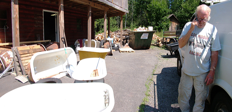 Mr. Tubs, surrounded by unrestored bathtubs takes a call outside his workshop. (Photo by Ethan Andrews) Mr. Tubs, surrounded by unrestored bathtubs takes a call outside his workshop. (Photo by Ethan Andrews)