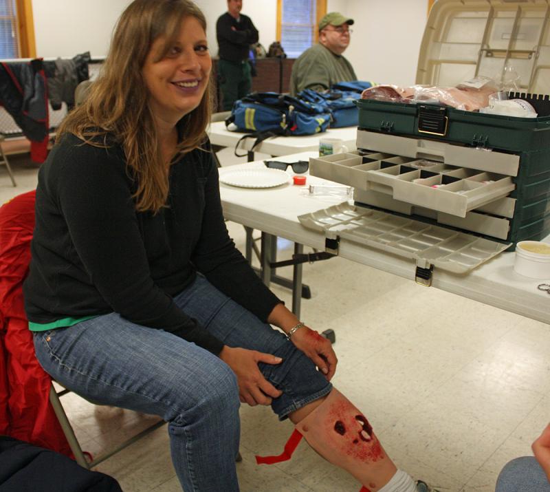 A volunteer "victim" shows off her newly applied moulage compound leg fracture and hypothermia-blue lip makeup. (Photo by Holly S. Edwards)