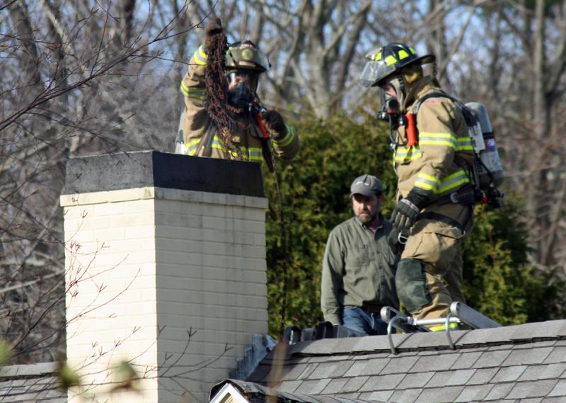 Camden firefighter Bob French Jr. chains smoldering debris down the chimney while Ryan Fisher looks on. (Photo by Holly S. Edwards)