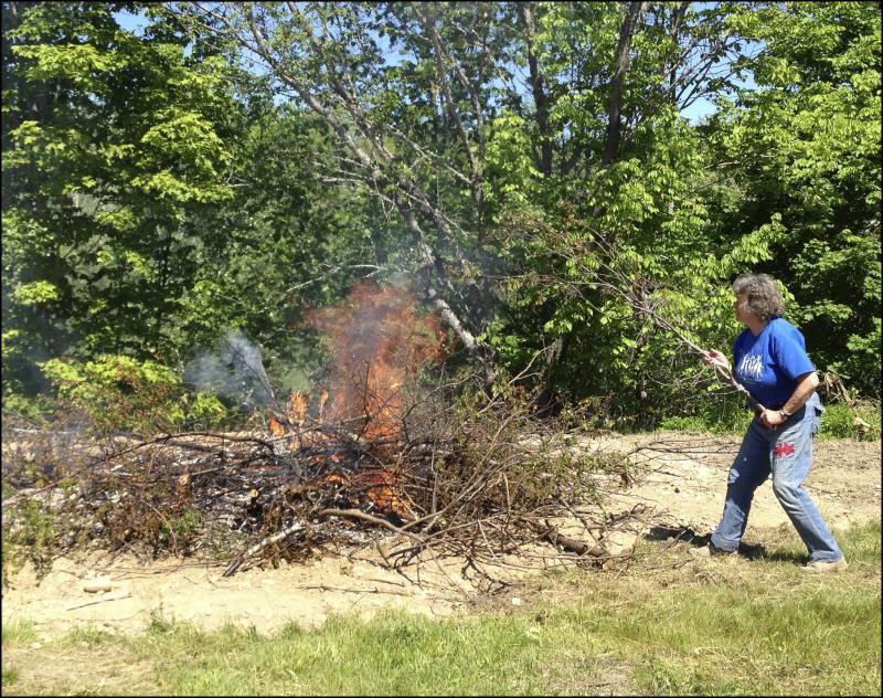 Diane O’Brien, chairman of the Lincolnville Historical Society, throws brush on the fire while helping to clear land for the society’s open-air museum next to the new library. (Photo by Sheila Polson)