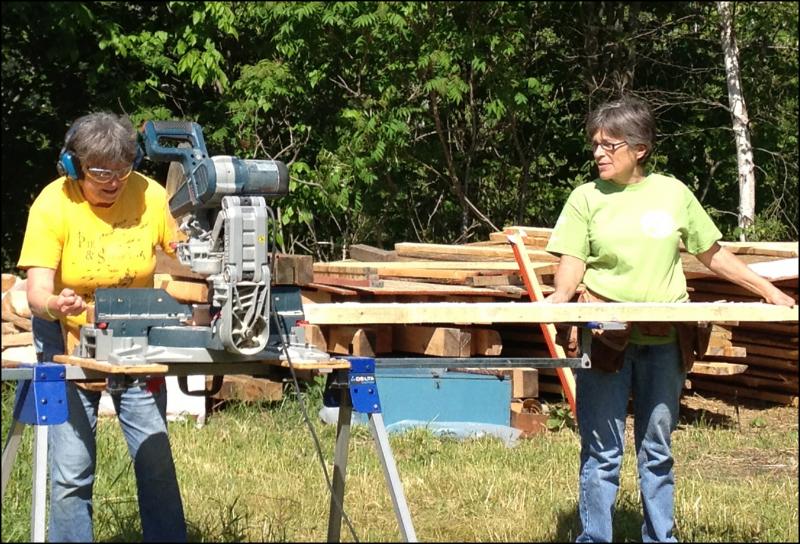 Diane O’Brien, chairman of the Lincolnville Historical Society, and Laurel Ames saw lumber for the floor joists on the open-air museum sheds. (Photo by Sheila Polson)
