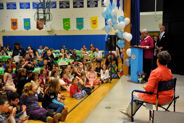 Carol Hathorne sitting in her personalized camp chair with many eyes on her, Ann Bresnahan speaking.