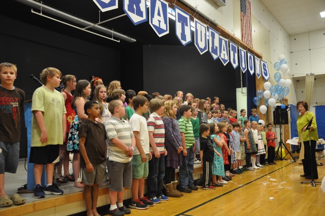 Shelly Burcalow directing the elementary school chorus singing a goodbye song.
