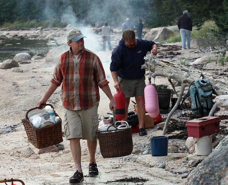 Schooner cook Rick Caroselli carries baskets of supplies while Capt. Barry King tidies the beach. (Photo by Holly S. Edwards)