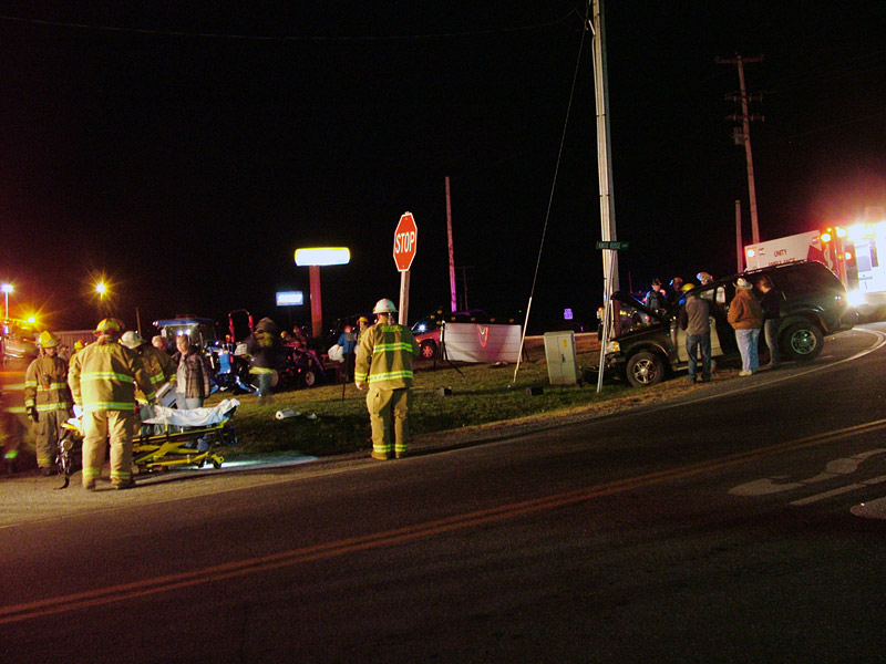 A view of the scene, looking across Route 220 (Knox Ridge South) from just south of the intersection with Route 137. The Ford SUV is visible at right. At left, emergency workers help one of the occupants of the vehicle onto a stretcher. (Photo by Ethan Andrews)