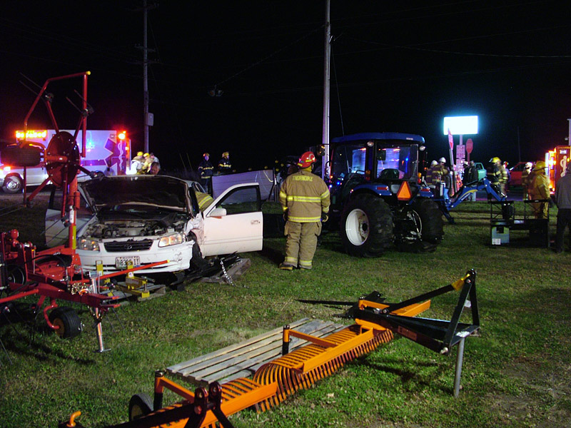 Emergency workers prepare to remove the driver from a car, left, that reportedly ran a stop sign at the intersection of Routes 137 and 220 in Knox and hit a westbound SUV. The SUV hit the utility pole visible in the background, while car came to rest amid farm equipment displayed outside Ingraham Equipment. (Photo by Ethan Andrews)