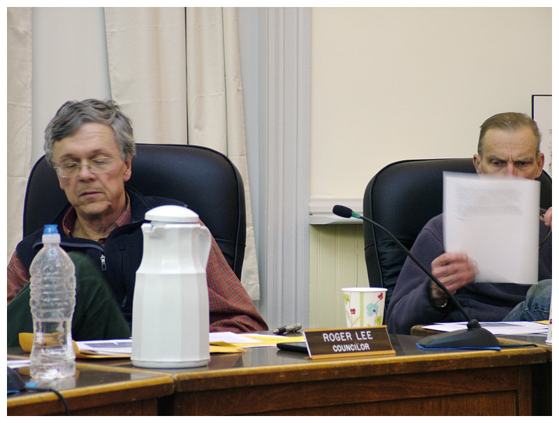 Councilors Roger Lee, left, and Eric Sanders both supported calling on the state to change its investments. There was some question among councilors about how the city’s view should be worded. Here, Sanders looks over a resolution drafted by a citizen group. (Photo by Ethan Andrews)