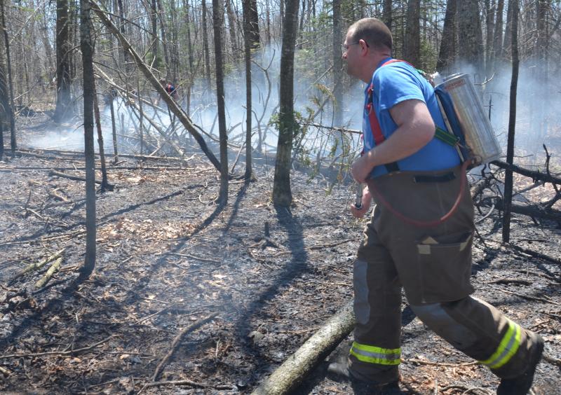 Rockport firefighter Neal Bartley works at extinguishing flames and smoldering underbrush during a woods fire May 8. (Photo by Lynda Clancy)