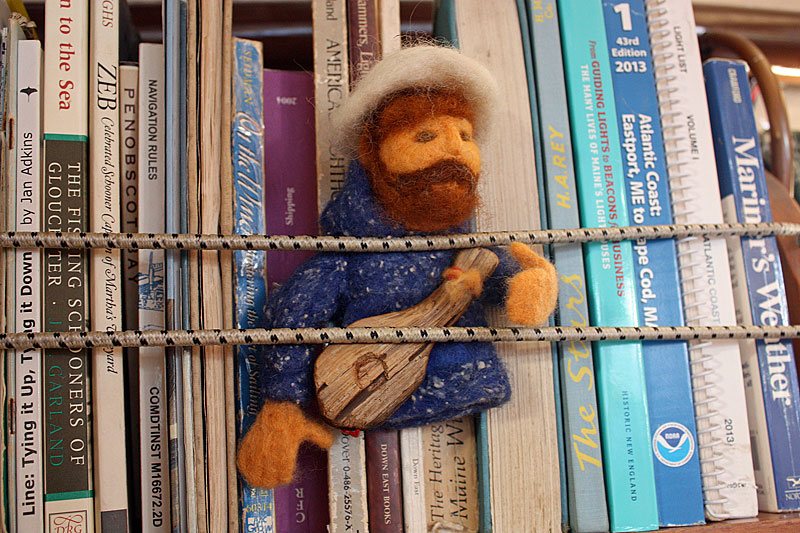 A Capt. Barry King felted doll, complete with a guitar, stands watch over the ship’s books. (Photo by Holly S. Edwards)