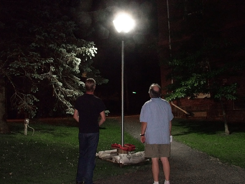 City councilors Eric Sanders, left, and Mike Hurley stand in front of a temporary lamp outside City Hall. The fixture is being used to test bulbs and lenses for new lighting in a section of downtown currently undergoing street and sidewalk renovations. Sanders likened the light from the test lamp to a UFO. (Photo by Ethan Andrews)