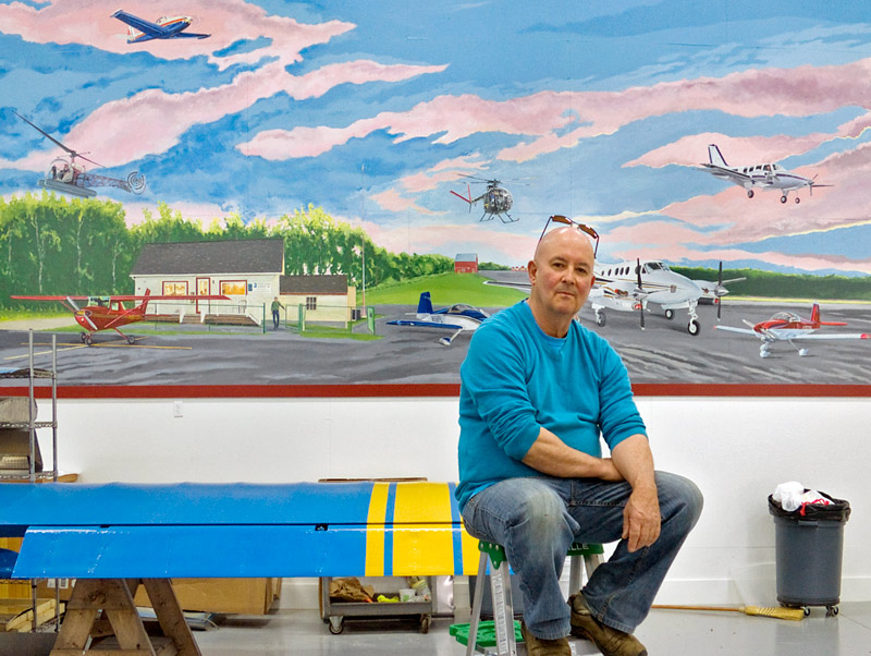 David Hurley in front of a mural he painted over the course of 7 months in an airplane hangar at Belfast Municipal Airport. (Photo by Ethan Andrews)