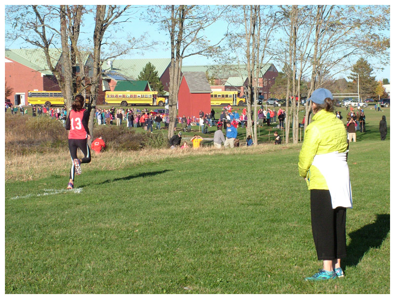 A coach watches a runner head into the final stretch. (Photo by Ethan Andrews)