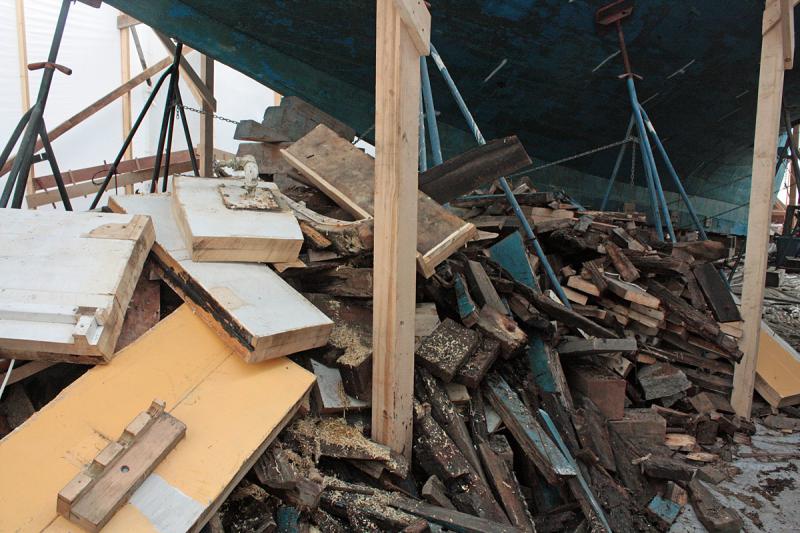 A pile of stripped rotted, broken wood and beams and other unneeded boards rests under the bow of the ‘Nathaniel Bowditch,’ while work has begun to completely rebuild the 1922 schooner. (Photo by Holly S. Edwards)