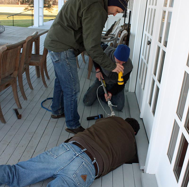 Evan Drinkwater works the pole, his dad, Kurt, reaches down into the hole to steady the net and Mike Sabatini shines the light while they work to hoist Lucy out of the hole in the foundation under the deck. (Photo by Holly S. Edwards)