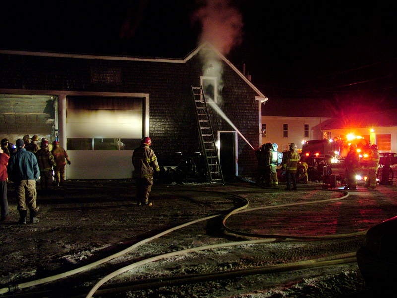 Firefighters pump water into the smoldering upper floor of a commercial building on Swan Lake Avenue in Monroe, Saturday night, while others inspect a garage at left. (Photo by Ethan Andrews)