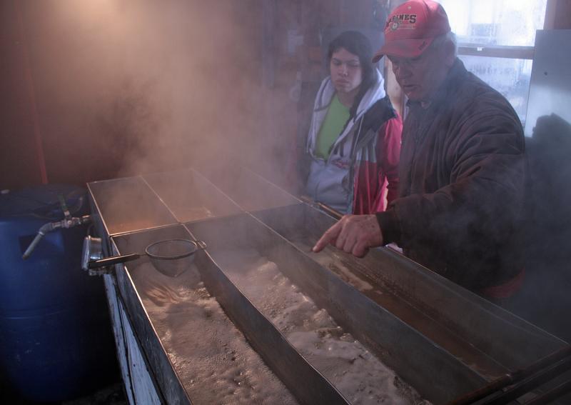 Skip Pound, right, explains the maple syrup extraction process to a visitor, Gabriella Blanco. (Photo by Holly S. Edwards)