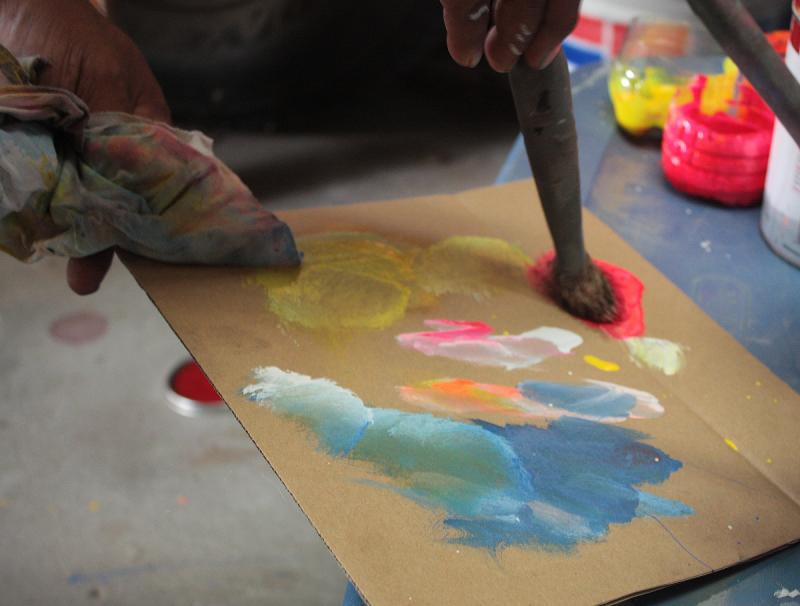 A piece of cardboard makes a fine paint pallet for Haider Ali. (Photo by Holly S. Edwards)