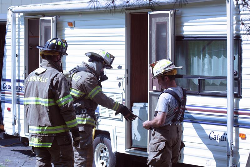 Lincolnville firefighters worked to remove a small refrigerator from inside Kergan Thomann’s camper, where a ruptured fuel line caused an explosion and small fire. (Photo by Holly S. Edwards)