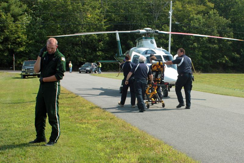 A LifeFlight of Maine crew member talks on the phone while Kergan Thomann, 29, of Lincolnville, is loaded into the helicopter to be flown to Portland for treatment of burn injuries he sustained Sunday around noon at his home. (Photo by Holly S. Edwards)