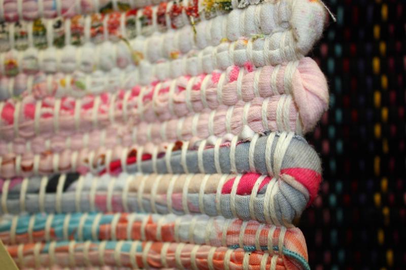 Details of a rag rug for sale, showing fabric strips woven with white ‘warp,’ which are the lengthwise yarns that are held in tension on a frame.