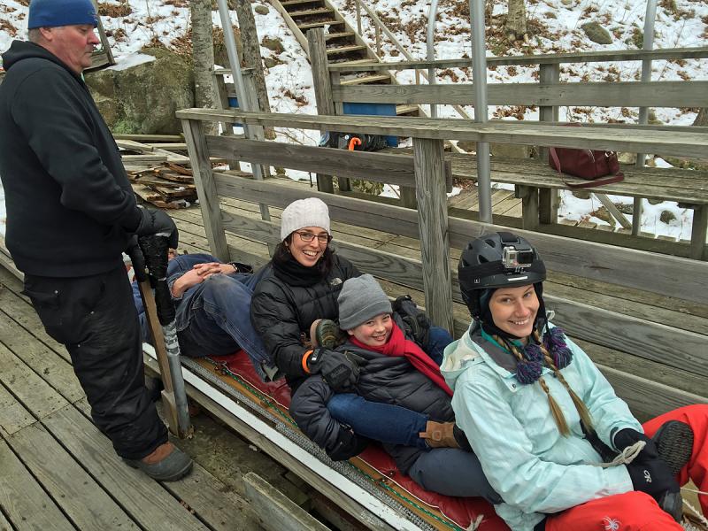 Bangor Daily News outdoor reporter Aislinn Sarnacki sits at the front of the toboggan Jan. 29, with Cute Potato blogger Jen Hazard and her daughter sandwiched in the middle. At the back, for ballast, is Toboggan Committee member and veteran racer Jim Jefferson, while Chute Master Stuart Young stands at the ready to release the sled into the chute. (Photo by Holly S. Edwards)