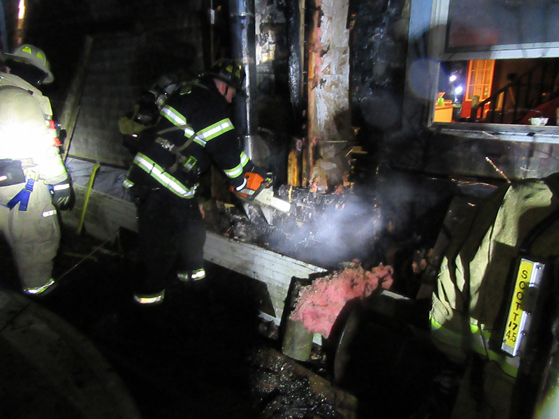 A Rockland firefighter cuts through the wall of the house on Winding Way Saturday night, during work to extinguish a fire there. (Courtesy Rockport Fire Department)