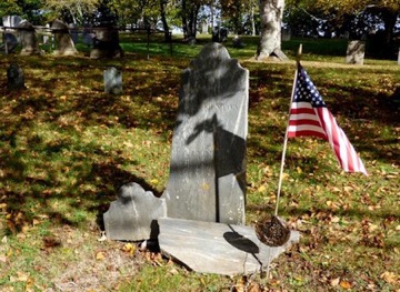 Kate Marshall, (not shown) of Nevada, came to Tolman Cemetery to view her Patriot ancestor’s grave. She found the gravestone of Benjamin Blackington (1749-1812) in several pieces, broken away from the double headstone with his wife, Eunice Woodcock (1743-1815). The image by Carl Mahoney shows the stone awaiting restoration and reuniting.