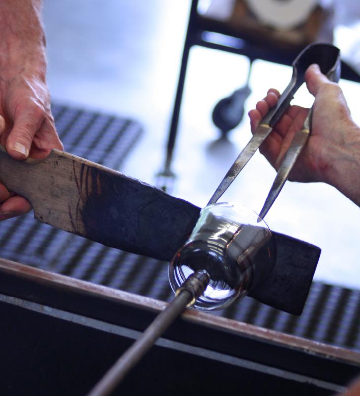 While one person spins the hot glass, another uses a paddle to smooth and even the drinking edge, or in this case the colored lip wrap. (Photo by Holly S. Edwards)