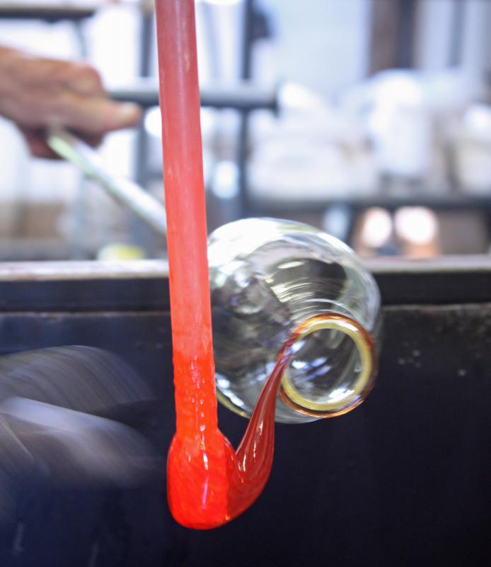 The glass is slowly turned with the colored molten glass lip wrap is attached around what will be the top, drinking edge of the finished glass. (Photo by Holly S. Edwards)