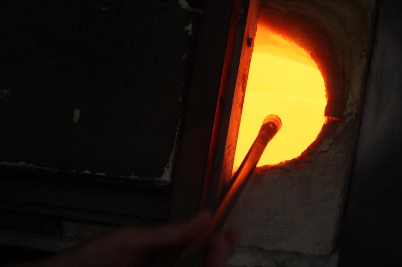 The crucible of molten glass is 2,170 degrees Fahrenheit, and the moment the glass is removed from inside, it immediately begins to cool and is reheated to a working temperature of around 1,800 F in the glory hole furnace. (Photo by Holly S. Edwards)