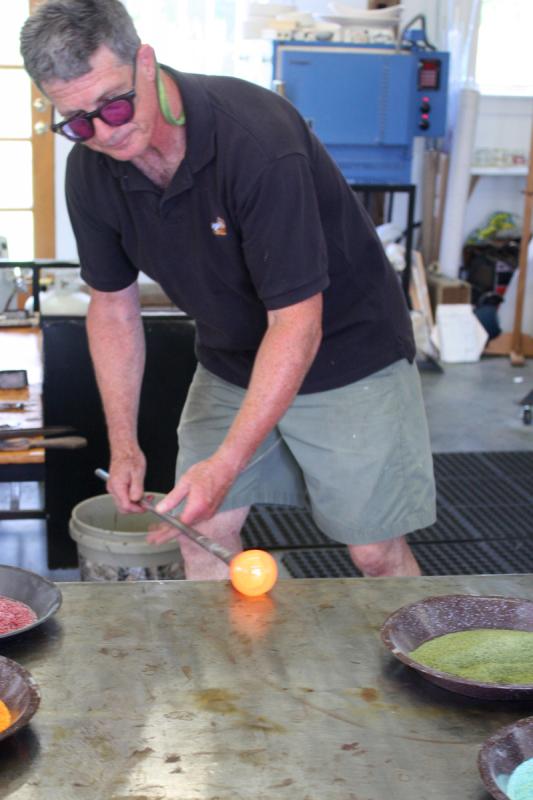Using the marver, a stainless steel table, David Jacobson begins the process of making a drinking glass by pushing and rolling the hot glass into a cone shape. (Photo by Holly S. Edwards)