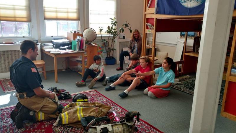 Firefighter Matt Heath demonstrates safety equipment, including his turnout gear and self-contained breathing apparatus, to a group of Montessori students. (Photo by Chris Farley)
