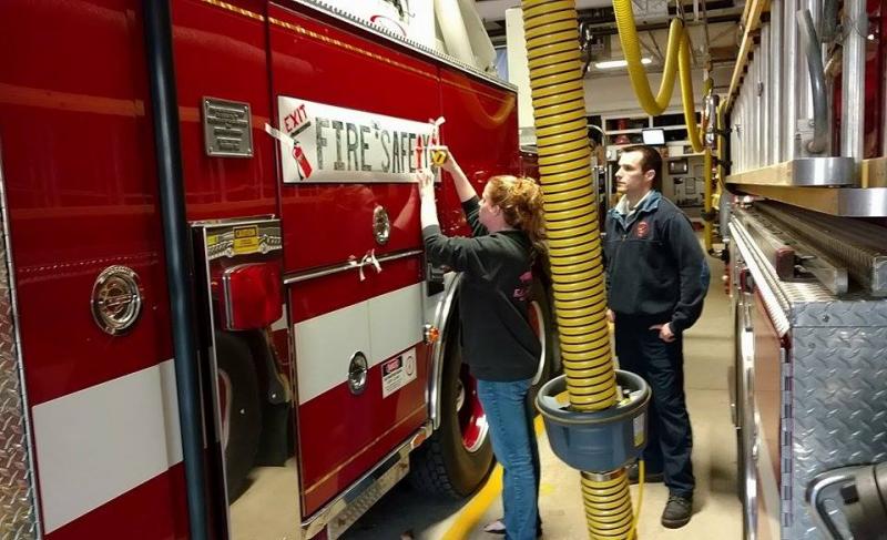 Rachel Pette of Adventure Advertising in Rockport works with Matt Heath, firefighter, to secure one of the winning logo banners on Camden’s ladder truck. (Photo by Chris Farley)