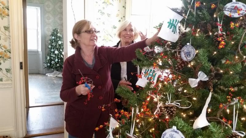 Mary Kay Felton and Susan Freeman, of the Lady Knox Chapter of Daughters of the American Revolution, decorate a holiday tree in the dining room featuring miniature ornaments that are replicas of the china used by General Henry and Lucy Knox. (Photo by Sarah Shepherd)