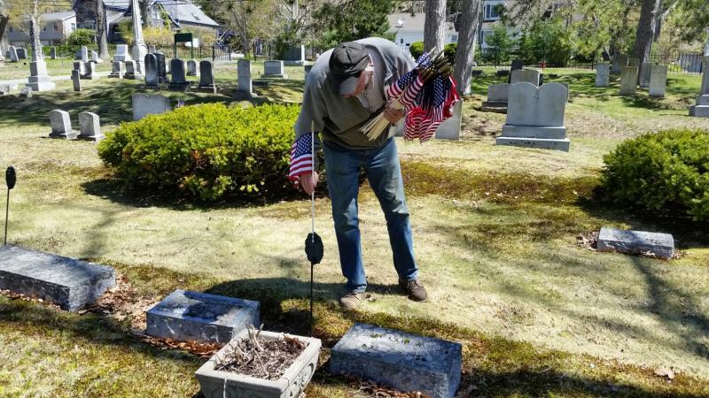 Rosey Gerry places a flag in a memorial marker at a veteran’s headstone in Mountain View Cemetery in Camden. (Photo by Sarah Shepherd)